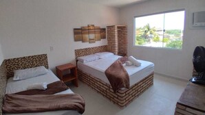 Ein Zimmer mit zwei Betten, einer Ziegelwand, einem kleinen Tisch, einem Fenster mit Aussicht und einem Deckenventilator.
