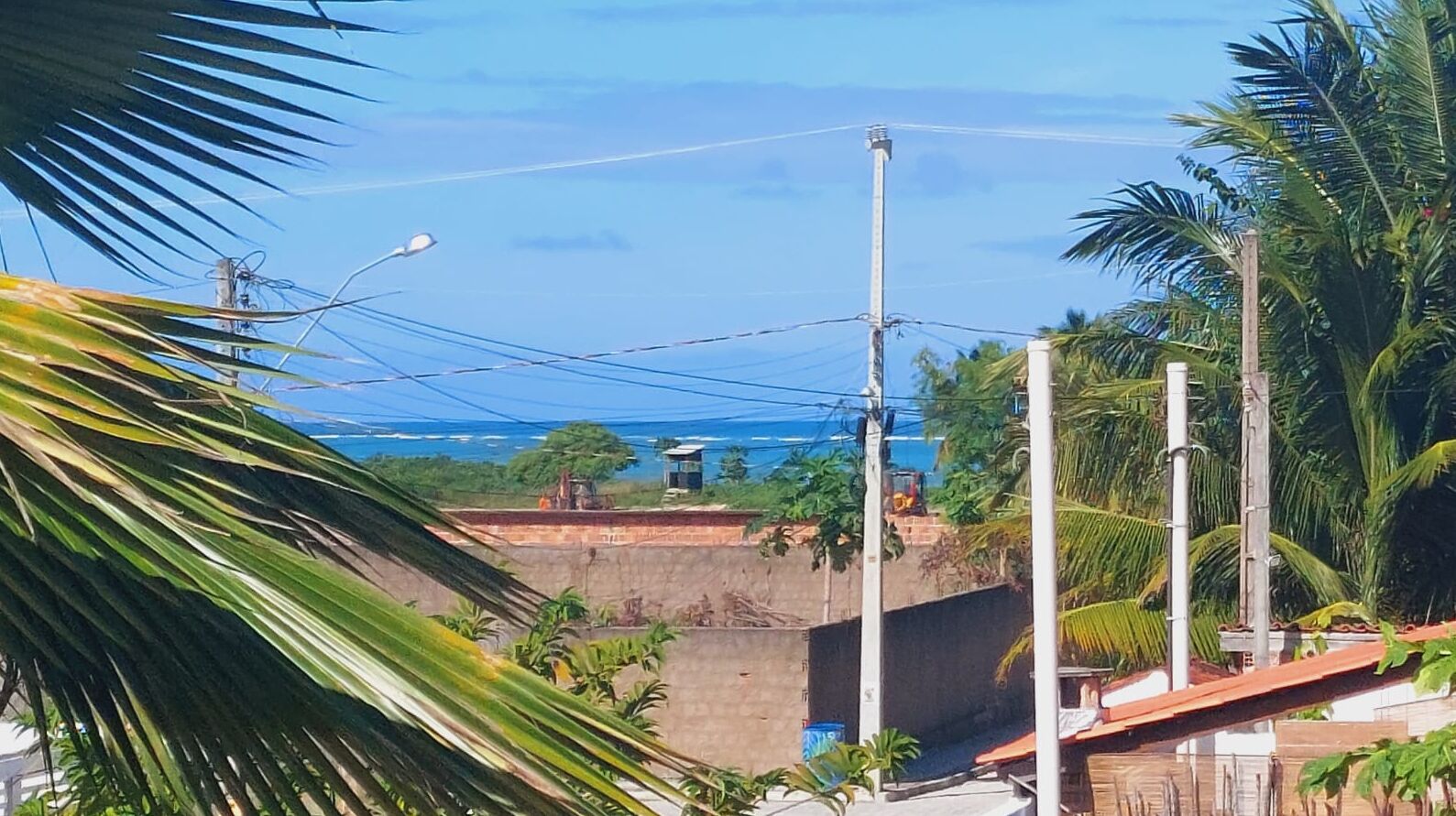 A residential area with a view of the ocean, palm trees, and a construction site in the background.