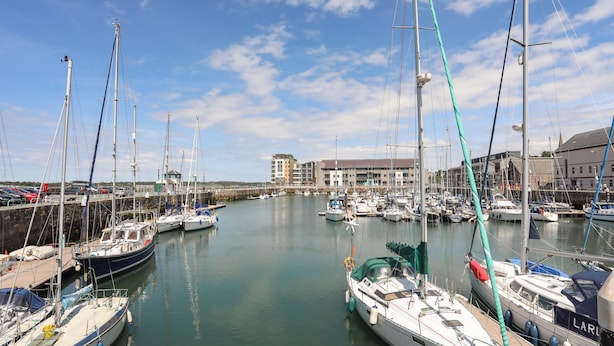 A marina with multiple boats docked, a clear sky, and buildings in the background. - Cwm Gwyrfai (Caernarfon)
