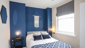 A bedroom with a bed, two bedside tables, a macrame wall hanging, and a window with a blind. - Cwm Gwyrfai (Caernarfon)