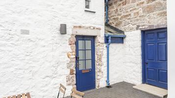 A white building with a blue door labeled "CWM GWYRFAL" and a blue door on the right. There is a bench and a small step leading to the door.
