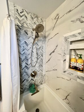 Ein Badezimmer mit Dusche, Handtuchhalter und Ablagefläche mit zwei Shampoo-Flaschen.