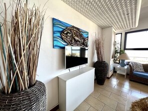 A modern living room with a flat-screen TV, a large abstract painting, and a large woven basket. - Hotel Giorgetti Palace (Bellaria)