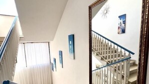 En gang med trappe, hvide vægge og et stort spejl der reflekterer trappen.