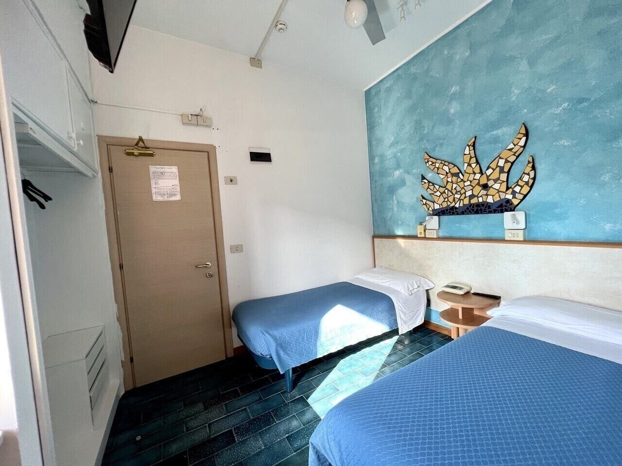A room with two beds, a door, a small table, and a wall decoration.
