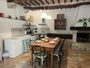 Une cuisine avec une table en bois dressée pour le repas, un réfrigérateur blanc et une cheminée en pierre.