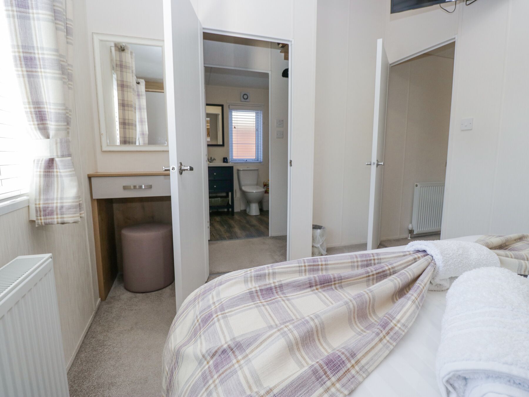 A bedroom with a bed, a bedside table, a radiator, and an open door leading to a bathroom.