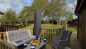 A deck with wicker furniture, a table with a bowl of food, and a large umbrella. - Lakeland Dream @ South Lakeland Leisure Lodge (Carnforth)