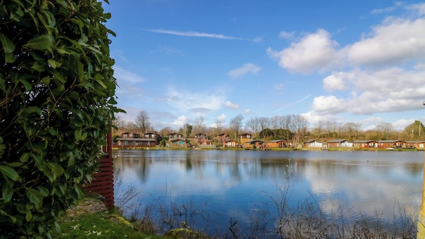 A lakeside view with wooden cabins and a grassy area. - Lakeland Dream @ South Lakeland Leisure Lodge (Carnforth)