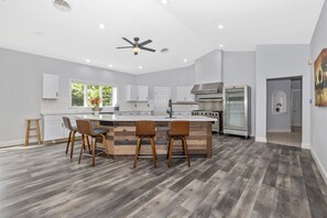 A modern kitchen with a central island, wooden chairs, and a ceiling fan.