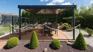 A covered outdoor seating area with tables and chairs, surrounded by a rope barrier and small conical bushes.