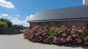 A stone building with a grey roof, surrounded by pink flowering bushes.