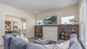A modern living room with a fireplace, a television, and a dining area visible through an open door.