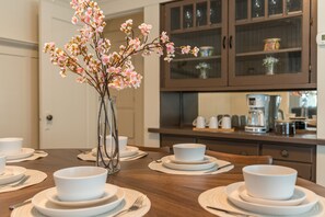 Enjoy meals in this beautifully set dining area with a wooden table, white plates, and a vase with fresh flowers.