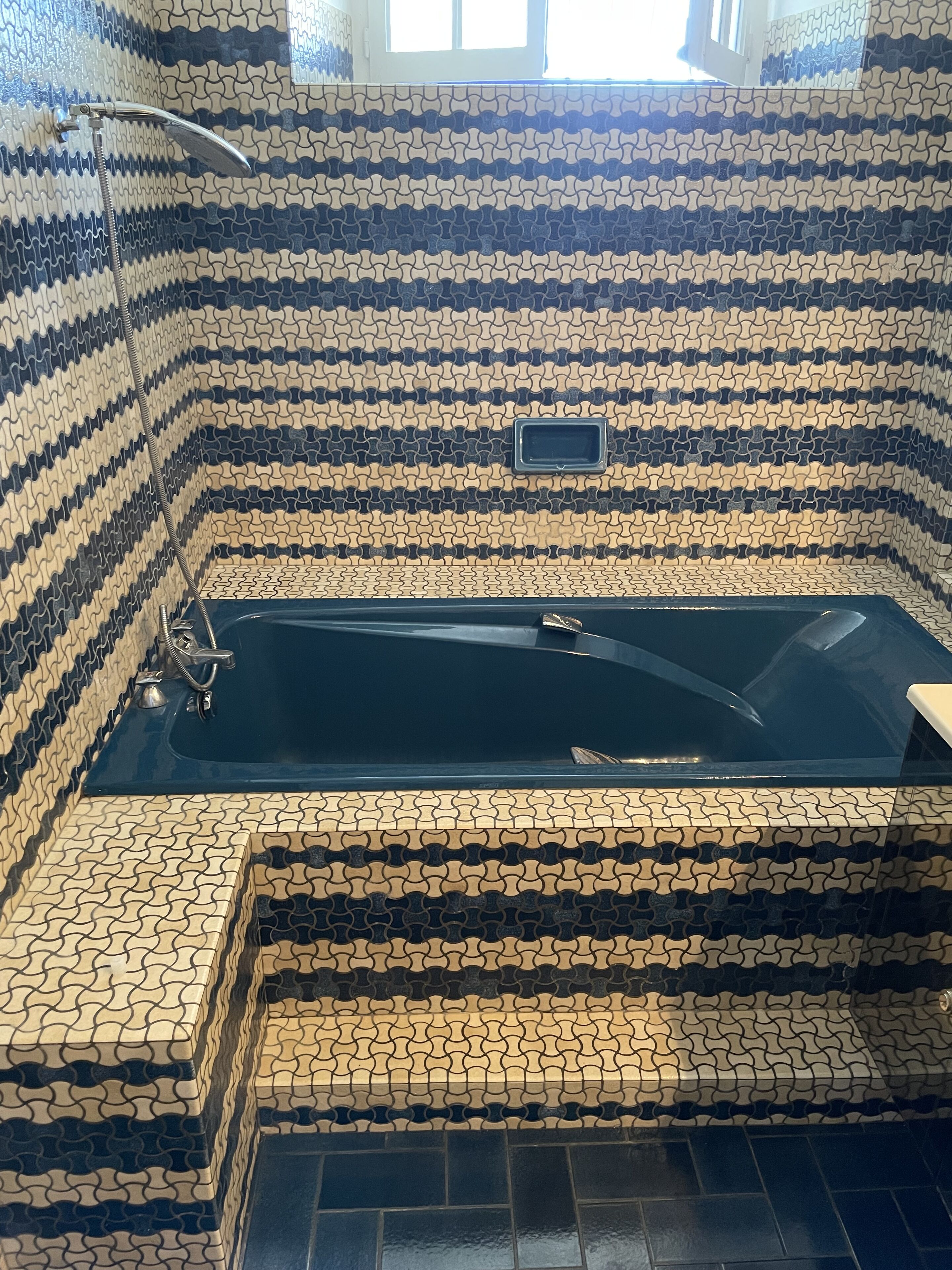 A bathroom with a black bathtub, a shower, and a tiled wall with a wavy pattern.