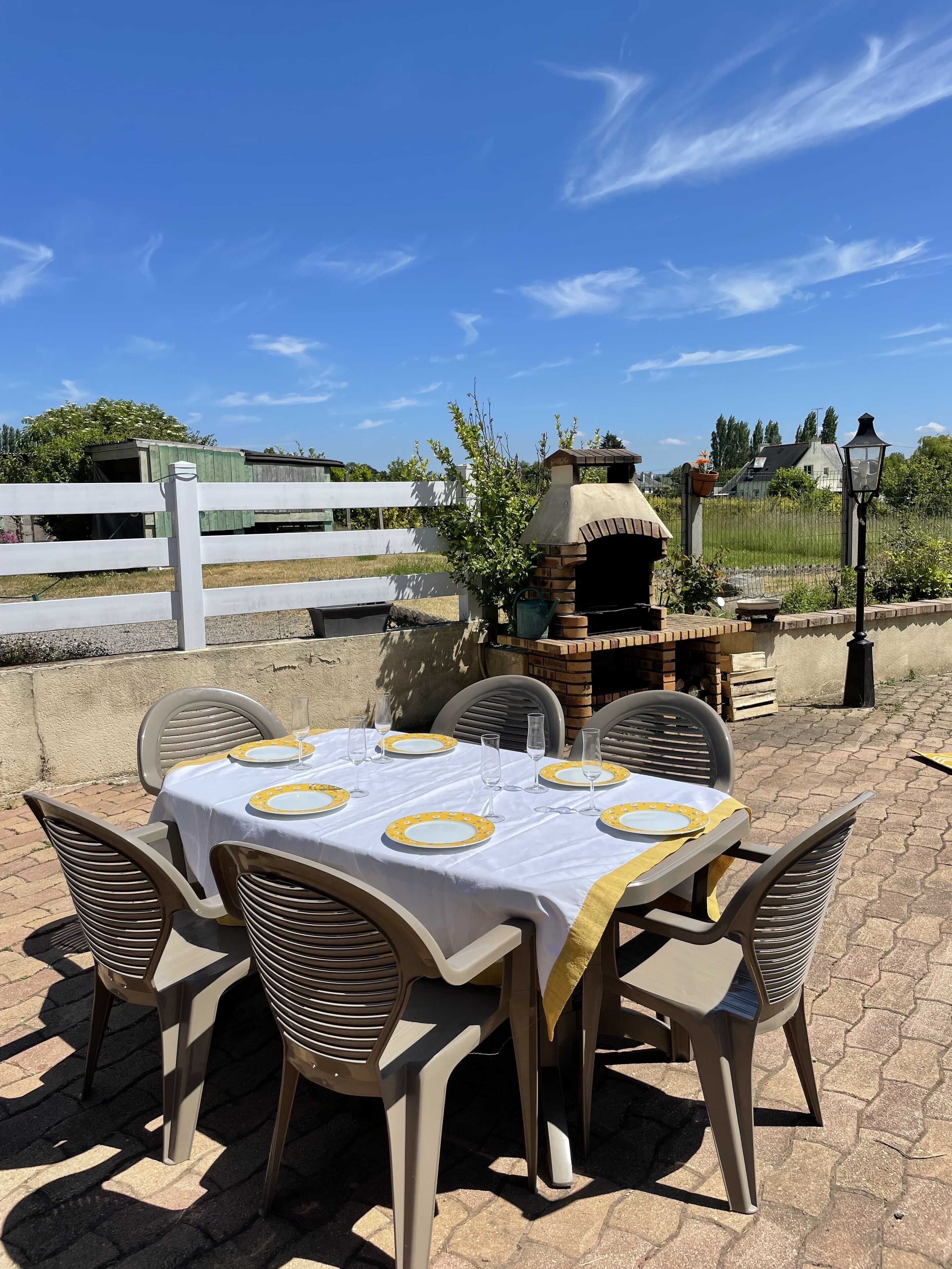 An outdoor dining area with a brick oven and a white fence in the background.