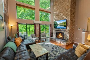 Un salón espacioso con chimenea de piedra, asientos confortables y grandes ventanales con vistas al exterior.