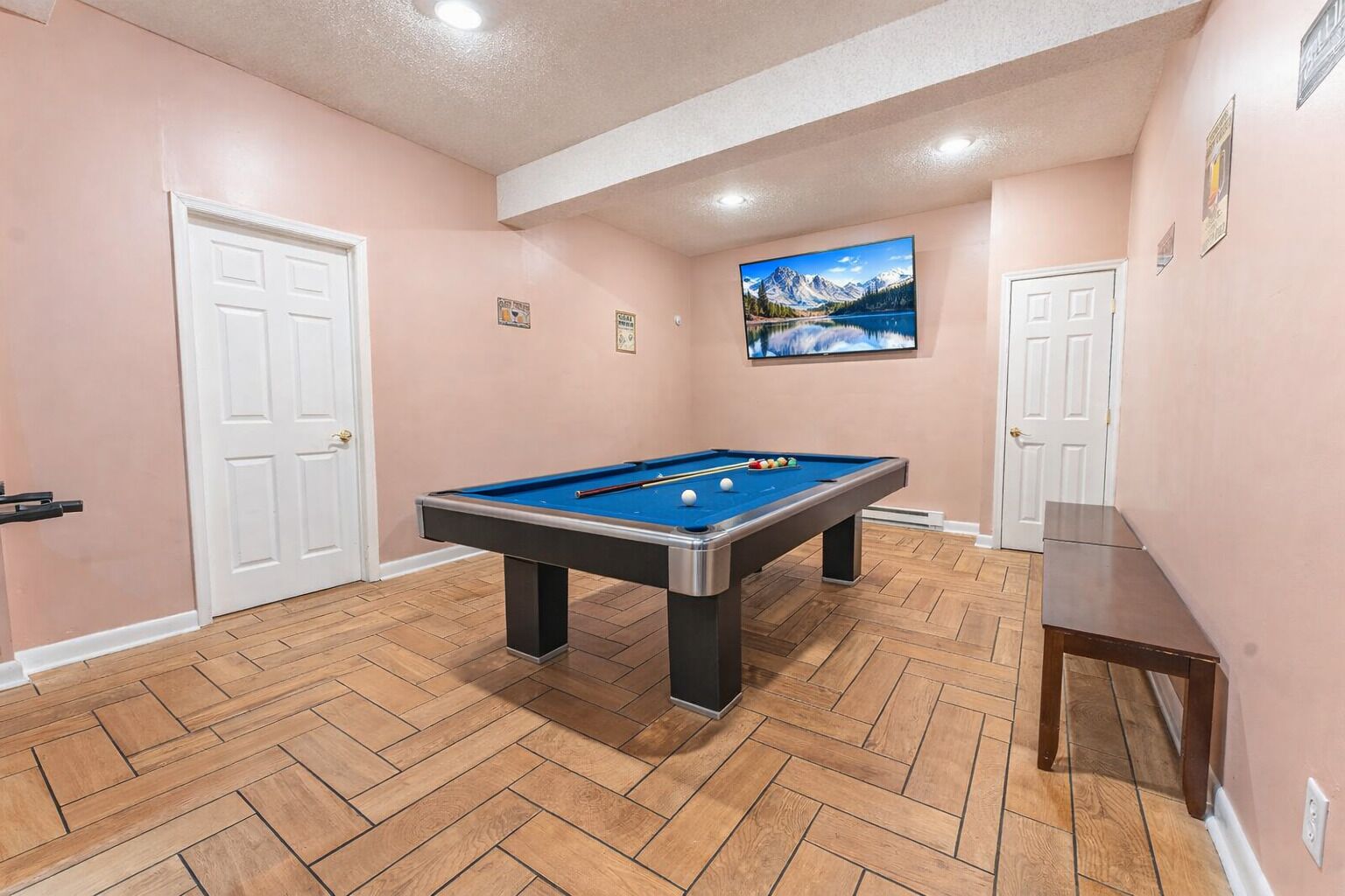 A pool table in a room with wooden flooring and pink walls.