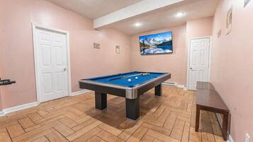 A pool table in a room with wooden flooring and pink walls.
