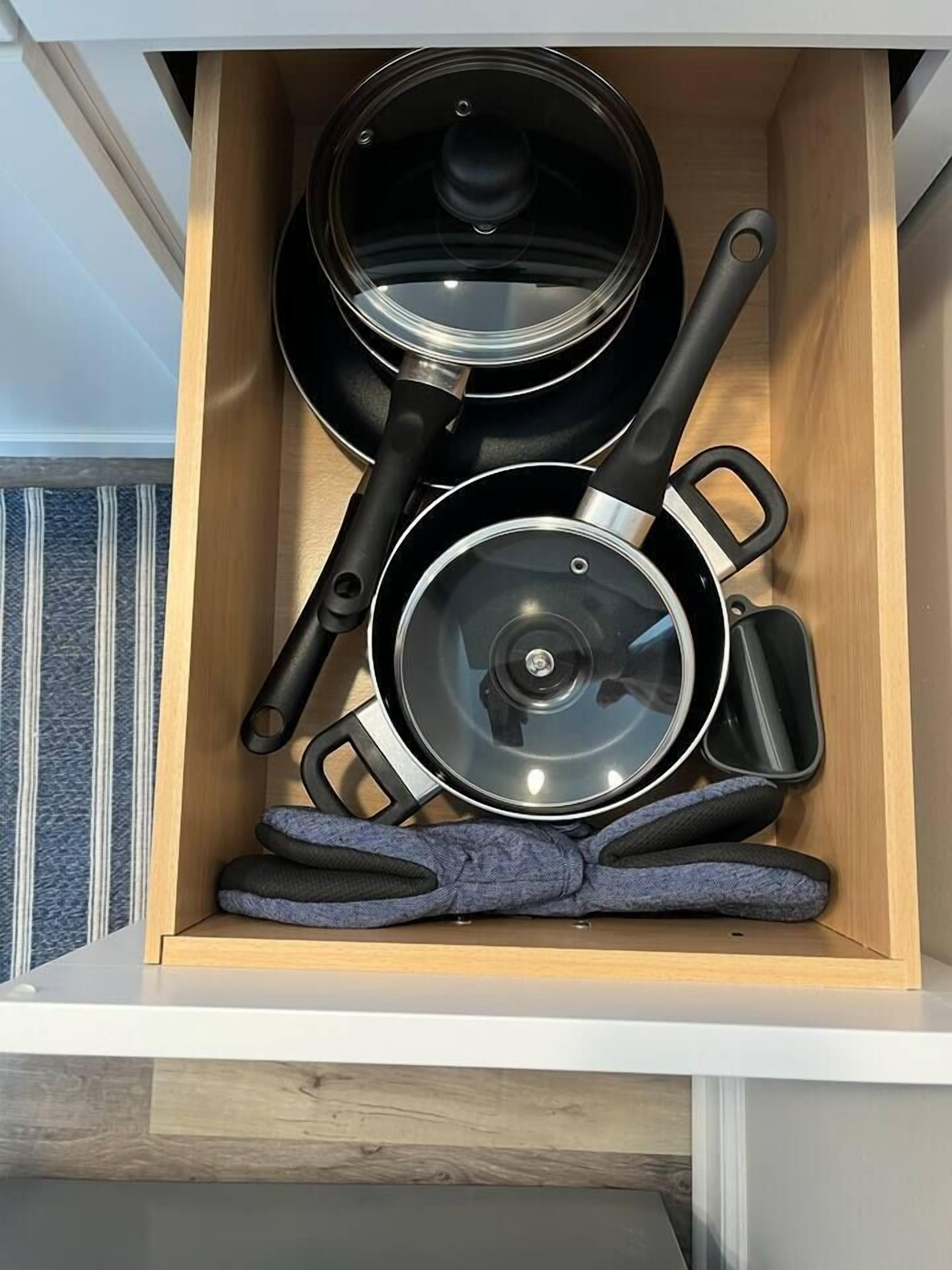 A drawer containing kitchen utensils including pots, pans, and oven mitts.