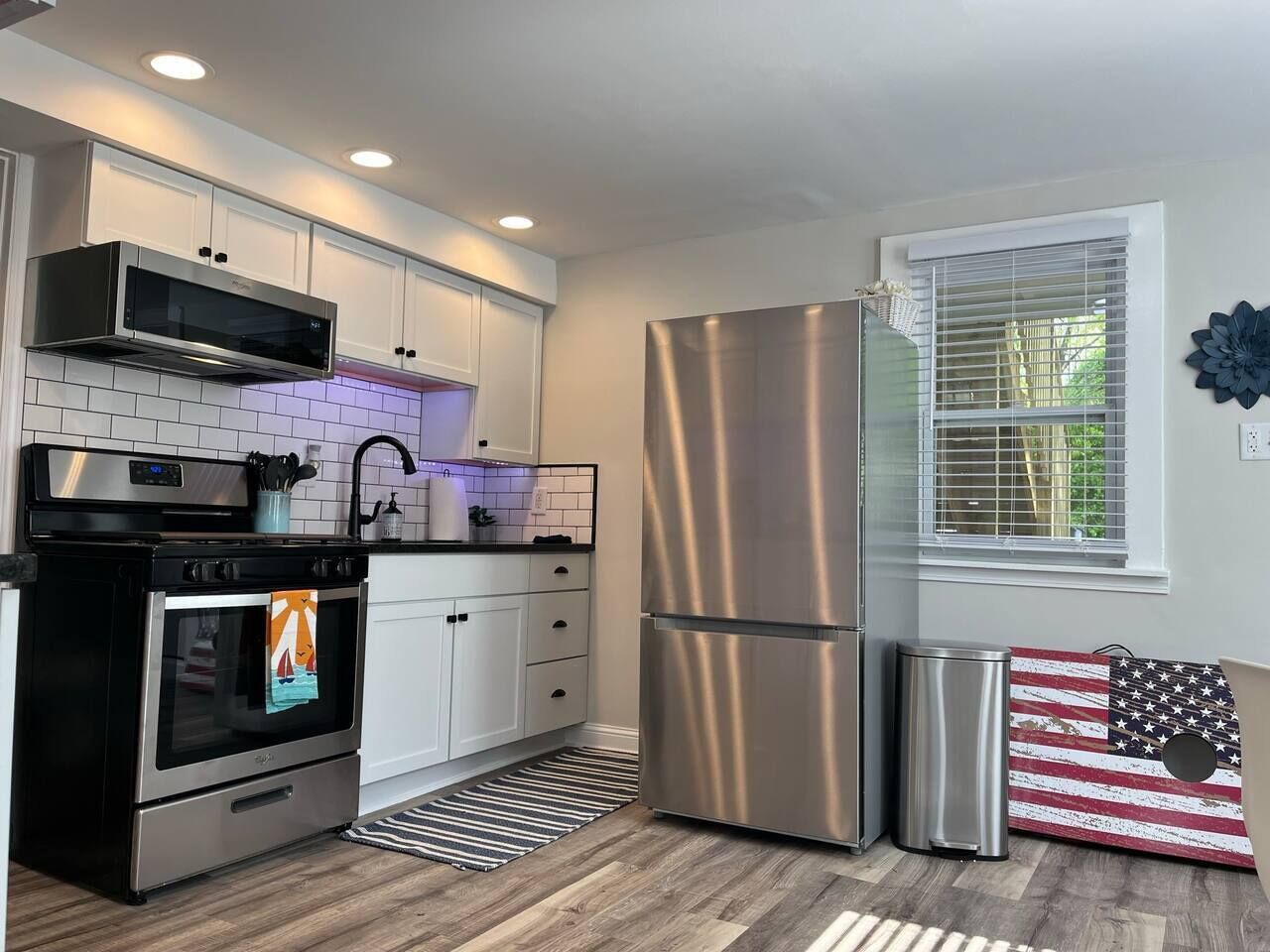 A modern kitchen with stainless steel appliances, white cabinetry, and a striped rug.