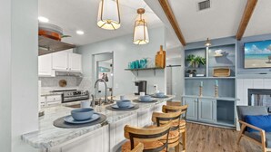 Cocina moderna con isla de mármol, sillas de madera e iluminación colgante.