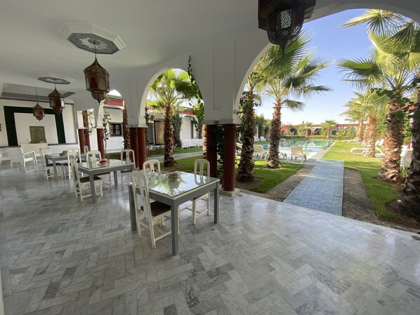 Amplio espacio interior con vista a la piscina, que incluye un comedor con mesas y sillas, y un techo con detalles decorativos.