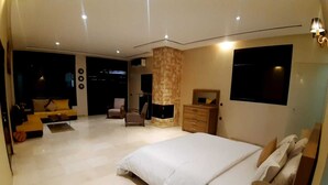 Een moderne slaapkamer met een groot bed, een houten dressoir, een zithoek met een bank en fauteuils, en een wand bekleed met steen.