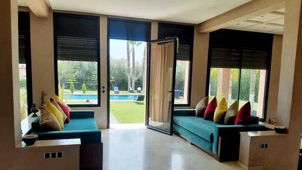 Een ruime woonkamer met een grote schuifpui naar een zwembad en tuin, twee banken met kussens, en een bijzettafeltje.