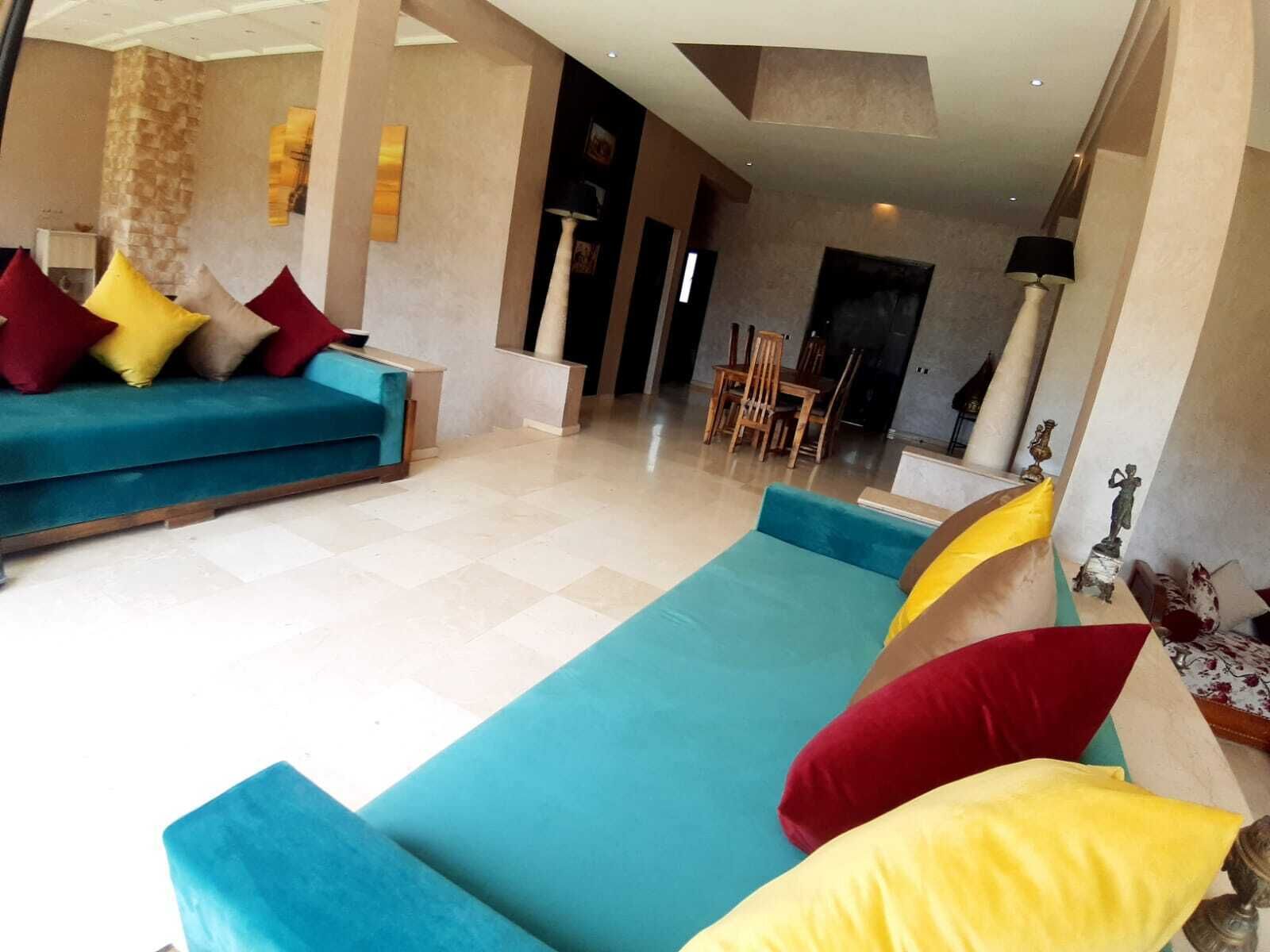 A spacious living area with a teal sofa set, a dining table with chairs, and a fireplace.