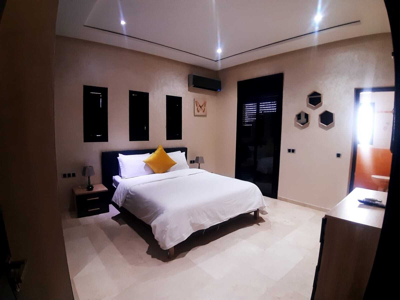 A modern bedroom with a large bed, a nightstand, a desk, and a door leading to a bathroom.