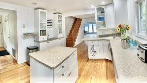 Una cocina moderna con armarios blancos, una isla central y una escalera de madera.