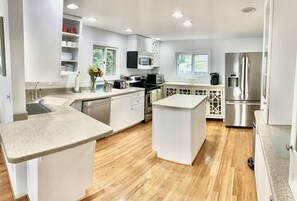 Una cocina moderna con armarios blancos, un refrigerador de acero inoxidable y piso de madera.
