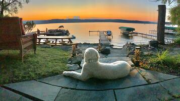 Een hond ontspant op een terras met uitzicht op een zonsondergang boven het water.