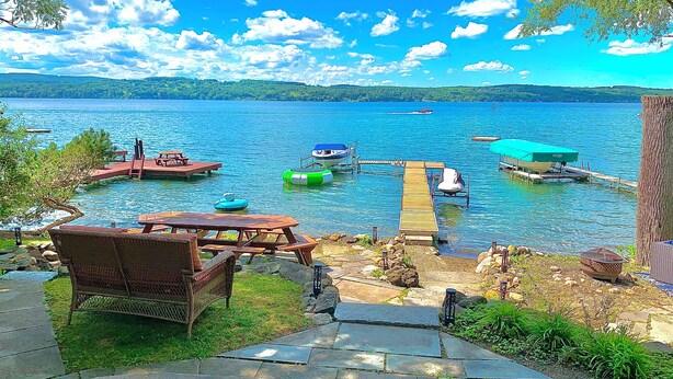 Terraza junto al lago con mesas de picnic, un muelle de madera y barcos.