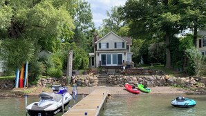 Un muelle con kayaks y un jet ski, un muro de piedra y una casa con terraza.