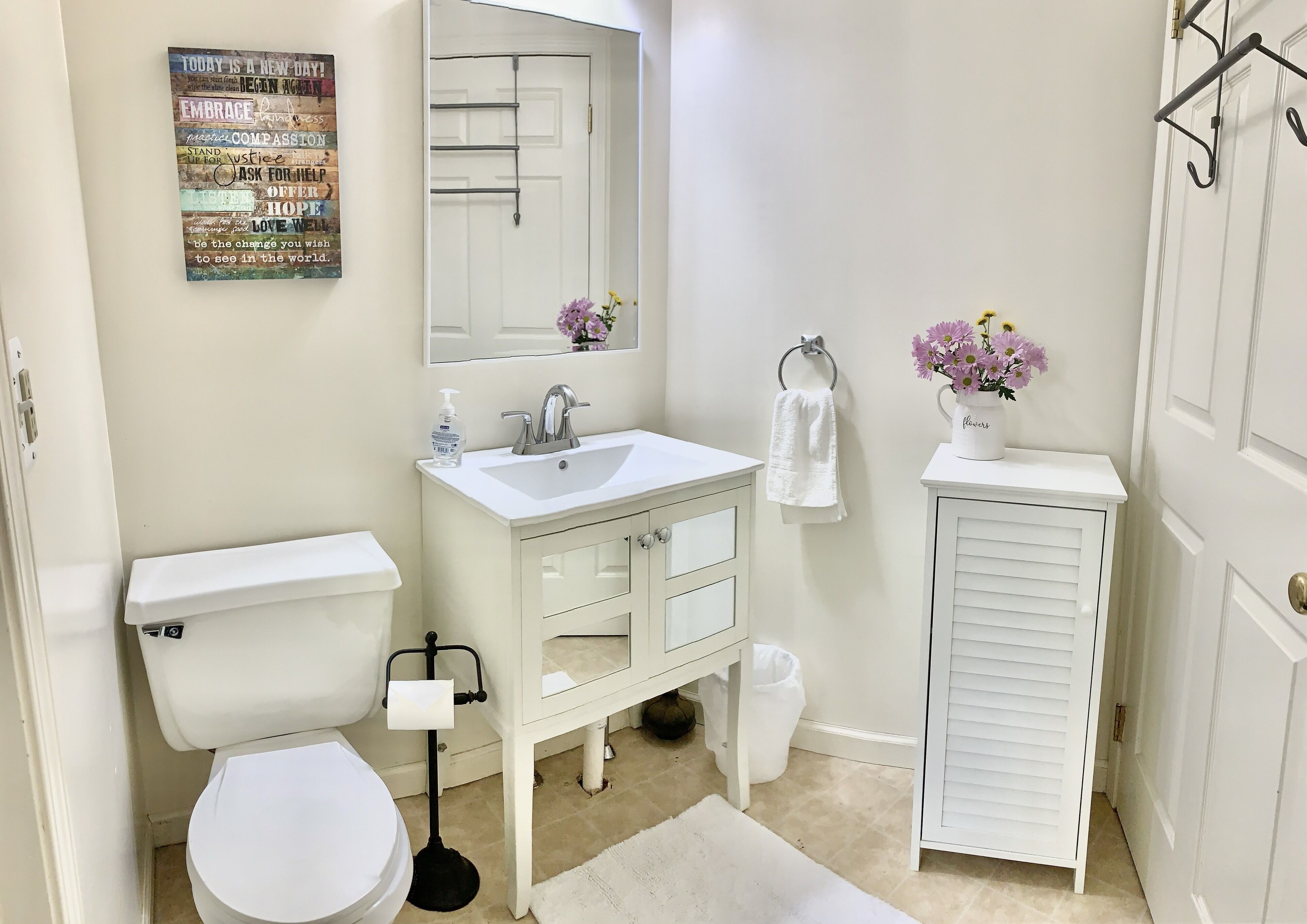 Un bagno con un water bianco, un lavandino e una cassettiera. Sopra il lavandino c'è uno specchio, un asciugamano su un portasci e un piccolo cestino.
