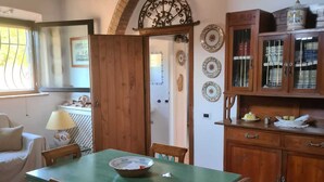 A dining area with a green table and wooden chairs, a wooden cabinet with dishes, and a tiled floor. - Wonderful Villa with garden in Ansedonia (Ansedonia)