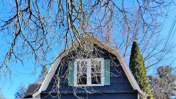 Une maison à deux étages avec des volets verts, une cheminée bien visible et une cour avant avec de la pelouse et une clôture.