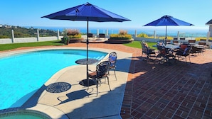 Ein Swimmingpool mit Liegestühlen und Sonnenschirmen, umgeben von einer Ziegelterrasse und Blick auf den Ozean.