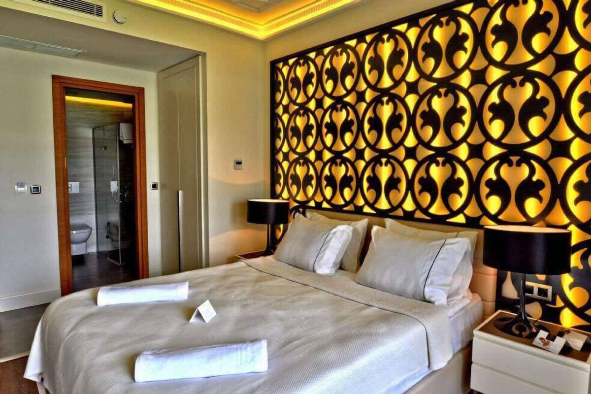 A hotel room with a large bed, a decorative wall panel, and a nightstand with a lamp.