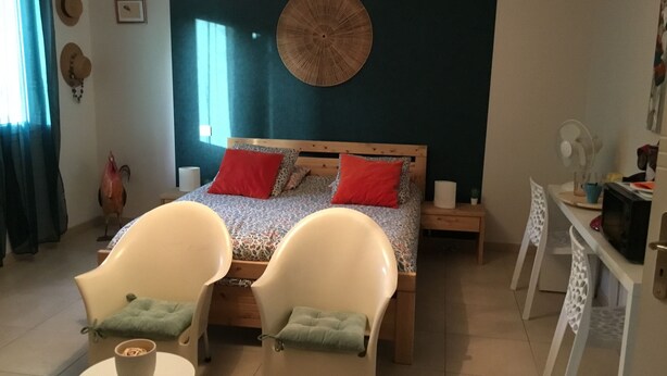 A bedroom with a bed, two chairs, a small table, a wall clock, a fan, and a decorative wall piece. - Room with private exit to small garden (Moussac)