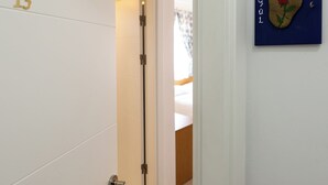 A hotel room with a wooden floor, a bed with a white headboard, and a door with the number 13. - Casa Gaia Otel (Bozcaada)