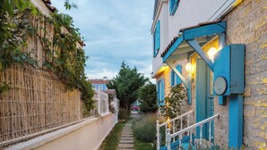 A narrow pathway leading to a building with blue shutters and a stone facade. - Casa Gaia Otel (Bozcaada)