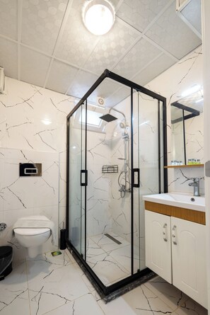 A modern bathroom with a glass-enclosed shower, white marble tiles, a white toilet, and a wooden vanity with a mirror. - Casa Gaia Otel (Bozcaada)