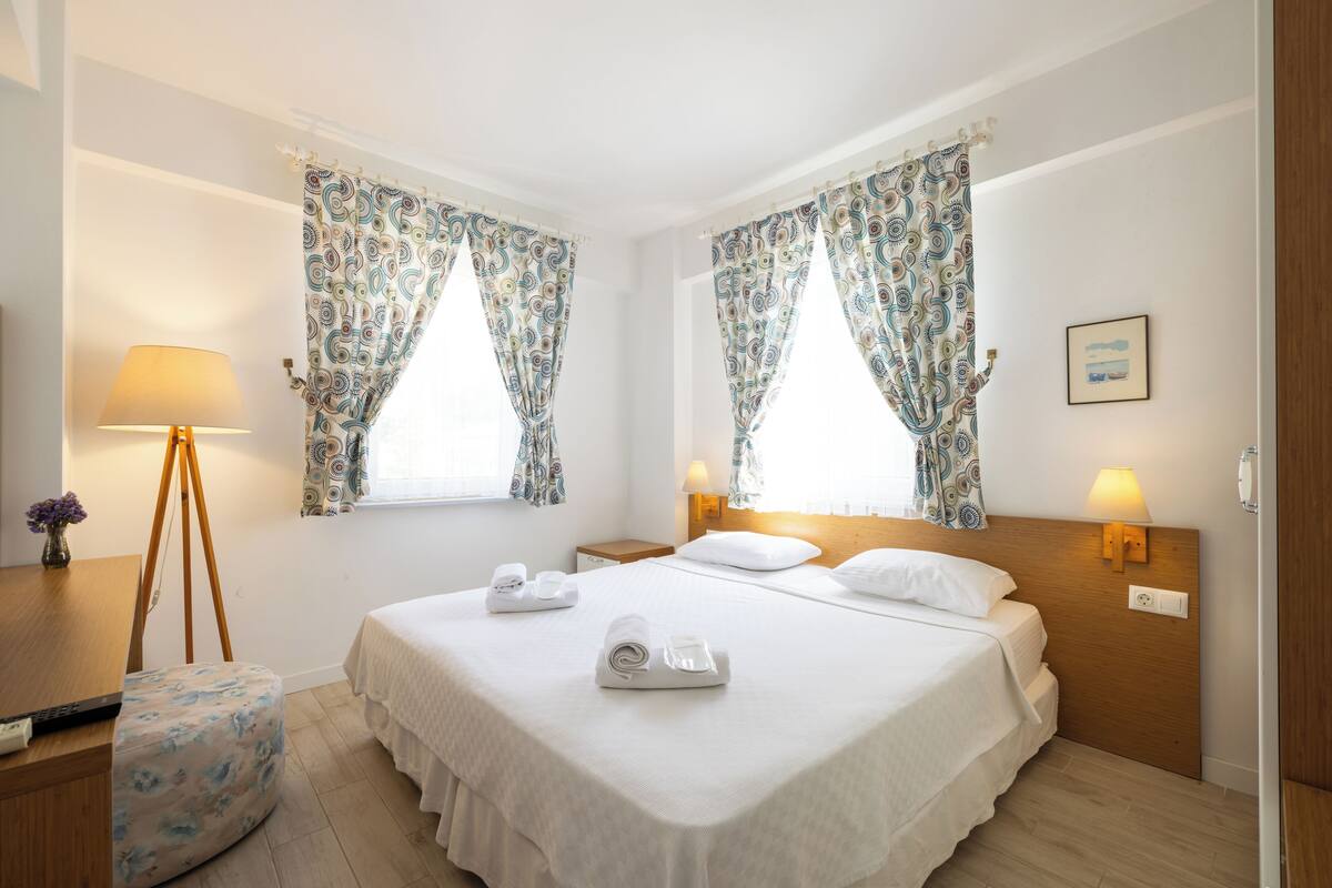 Habitación de hotel con dos camas, un escritorio con lámpara y una ventana con cortinas estampadas.