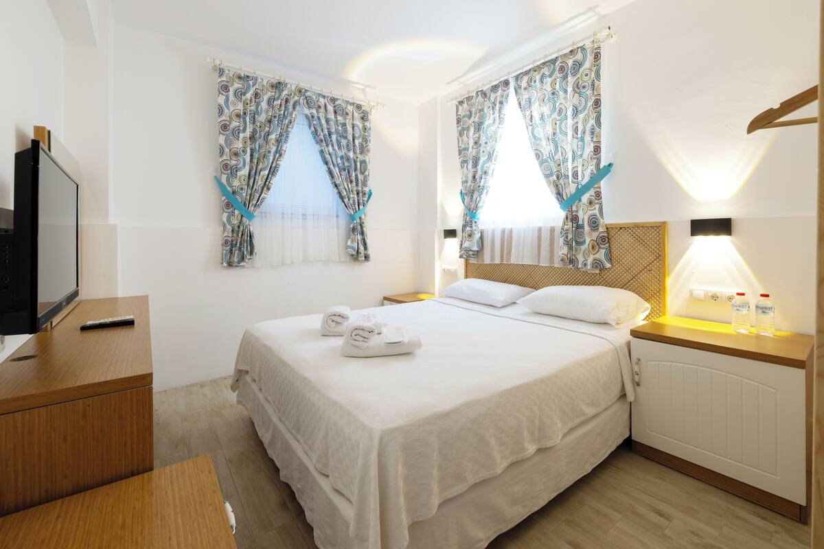 Una habitación de hotel con cama, mesitas de noche, televisión y cortinas.