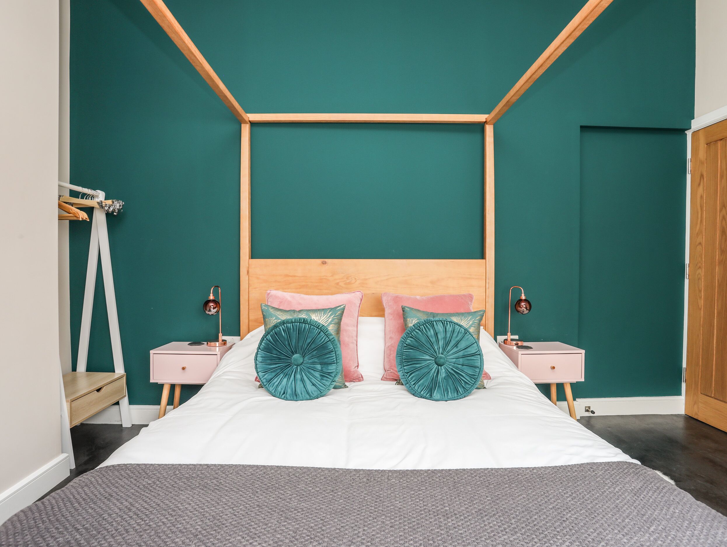 A neatly arranged bedroom with a wooden headboard, white bedding, and teal accent pillows.