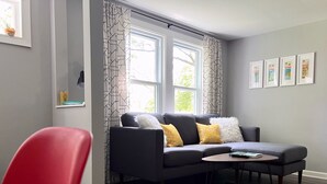 A modern living room with a grey sofa, a red chair, a round coffee table, and a black rug. - Near DT Madison - One Block from Lake Monona & Lake Loop Bike Path (Monona)