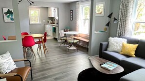 A modern living room with a grey sofa, a coffee table, and a dining area with red chairs and a white table. - Near DT Madison - One Block from Lake Monona & Lake Loop Bike Path (Monona)